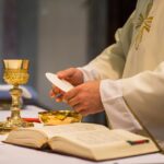 Mensagem dia Padre 2025. A imagem mostra um sacerdote consagrando a eucaristia durante a missa.