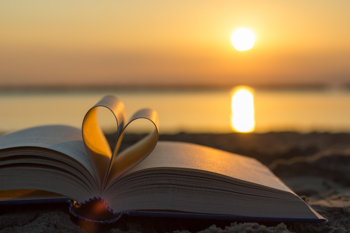 Amor de Deus. Um livro com as páginas dobradas em forma de coração e uma praia ao por do sol ao fundo.
