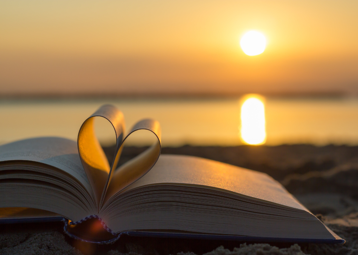 Amor de Deus. Um livro com as páginas dobradas em forma de coração e uma praia ao por do sol ao fundo.