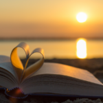 Amor de Deus. Um livro com as páginas dobradas em forma de coração e uma praia ao por do sol ao fundo.