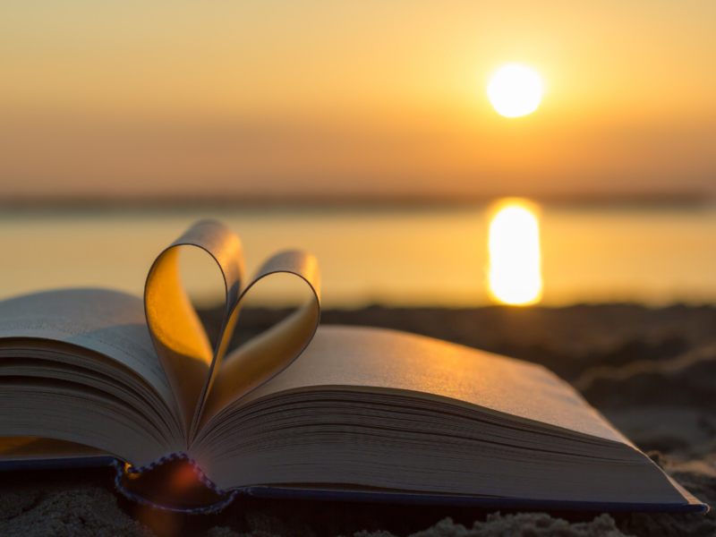 Amor de Deus. Um livro com as páginas dobradas em forma de coração e uma praia ao por do sol ao fundo.